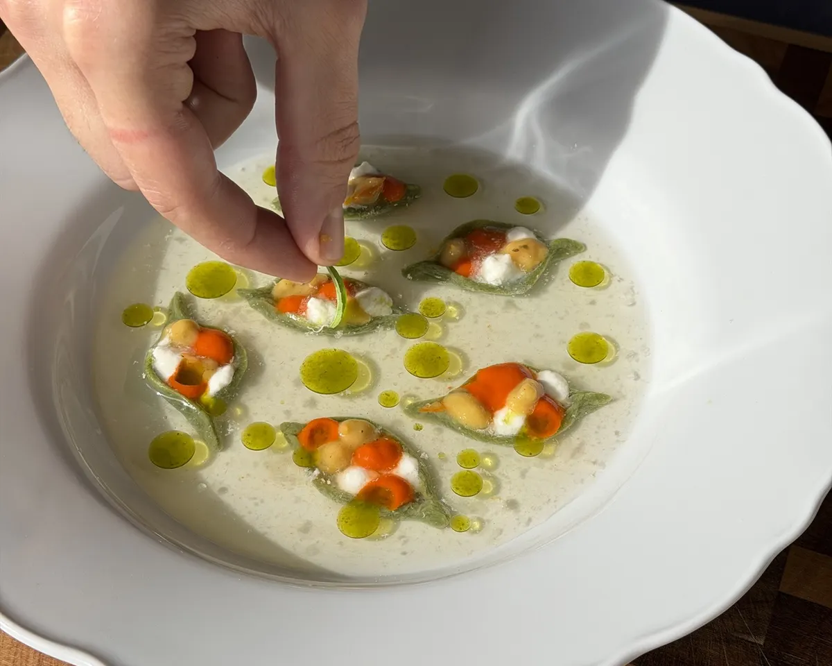 Hands plating filled pasta with herb oil